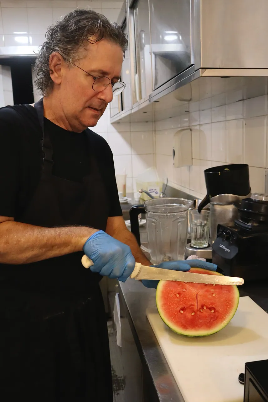 Funcionário a cortar uma melancia fresca na cozinha