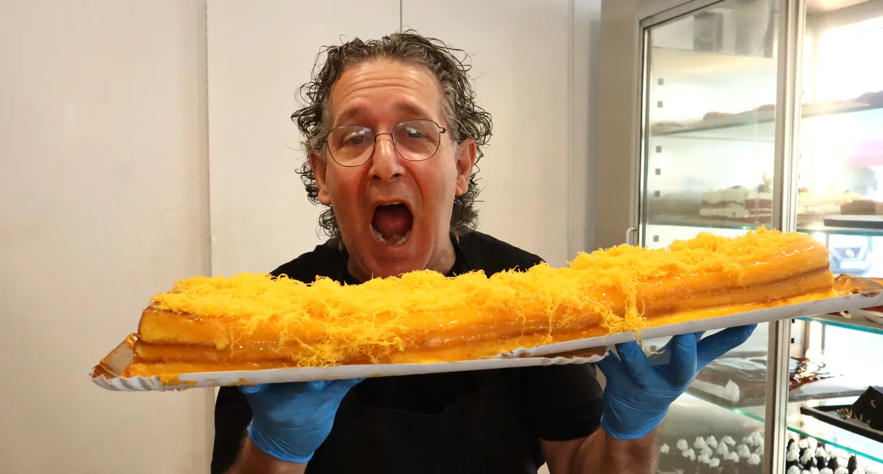 Funcionário a mostrar, orgulhoso, um bolo de laranja de um metro