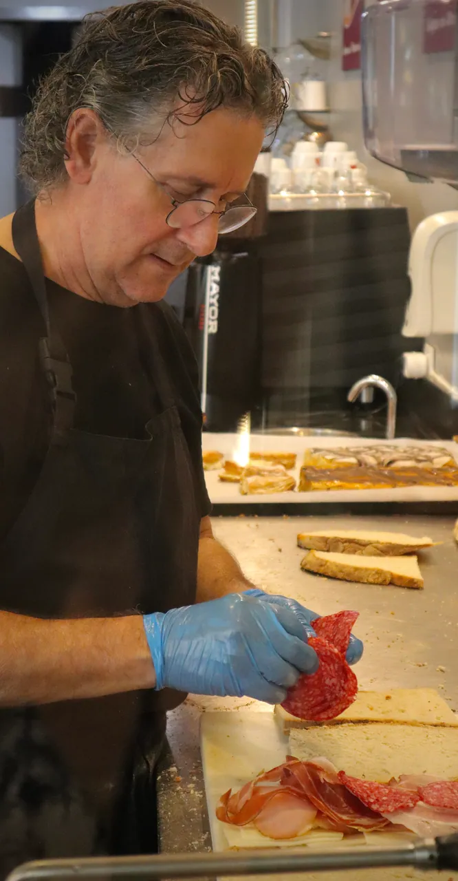 Funcionário a rechear uma tosta com enchidos, ao balcão